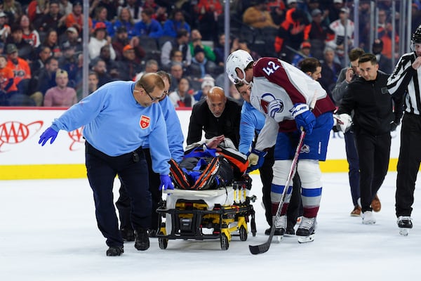 Colorado Avalanche's Josh Manson (42), right, talks to referee Mitch Dunning, center, as Dunning is stretchered off the ice after an injury during the first period of an NHL hockey game between the Philadelphia Flyers and the Avalanche, Monday, Nov. 18, 2024, in Philadelphia. (AP Photo/Derik Hamilton)