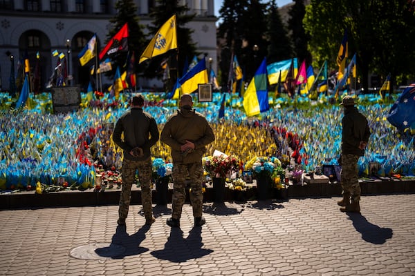 Ukrainian service men stand next to Ukrainian flags and photographs placed in memory of civilians and soldiers killed during the war, at the Independence square in central Kyiv, Saturday, April 20, 2024. (AP Photo/Francisco Seco)