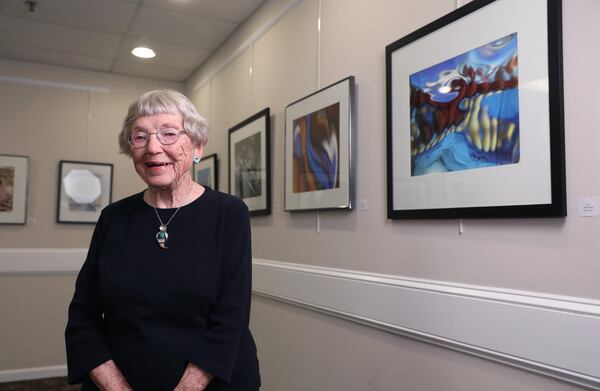 Ruth Gogel, who is 91, poses with her work in the gallery at Clairmont Place. Gogel, an accomplished photographer, led a project with fellow residents to put artwork up in the spaces inside Clairmont Place. Gogel does abstract photography capturing images of objects behind glass bricks. JASON GETZ / SPECIAL TO THE AJC