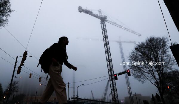 Sarah Cruz walks past foggy cranes on 17th Street in Midtown. According to Channel 2 Action News, the fog should lift by midmorning.