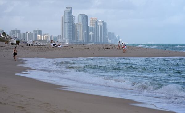 FILE - People walk along the beach in Surfside, Fla., near the skyline of Sunny Isles Beach, Dec. 17, 2024. (AP Photo/Lynne Sladky, file)