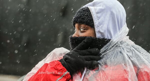 Trina Cloud, who works security, protects her face from the snow and sleet mix falling at Mercedes- Benz Stadium, where Georgia high school football is underway.