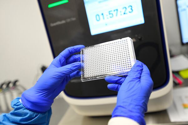 A lab worker holds a plate that will hold samples of possible COVID-19 and will be put in the machine behind it to be analyzed at Ipsum Diagnostics labratory on Monday, March 23, 2020.  (John Amis)