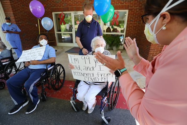 Westbury Medical Care & Rehab administrator Jennifer Vasil applauds then 99-year-old COVID-19 survivor Irma Gooden, who has since turned 100, and Johnny Simmons, 65, while preparing to hold a celebration for the recovery of some of the facility residents in May. CURTIS COMPTON / CCOMPTON@AJC.COM