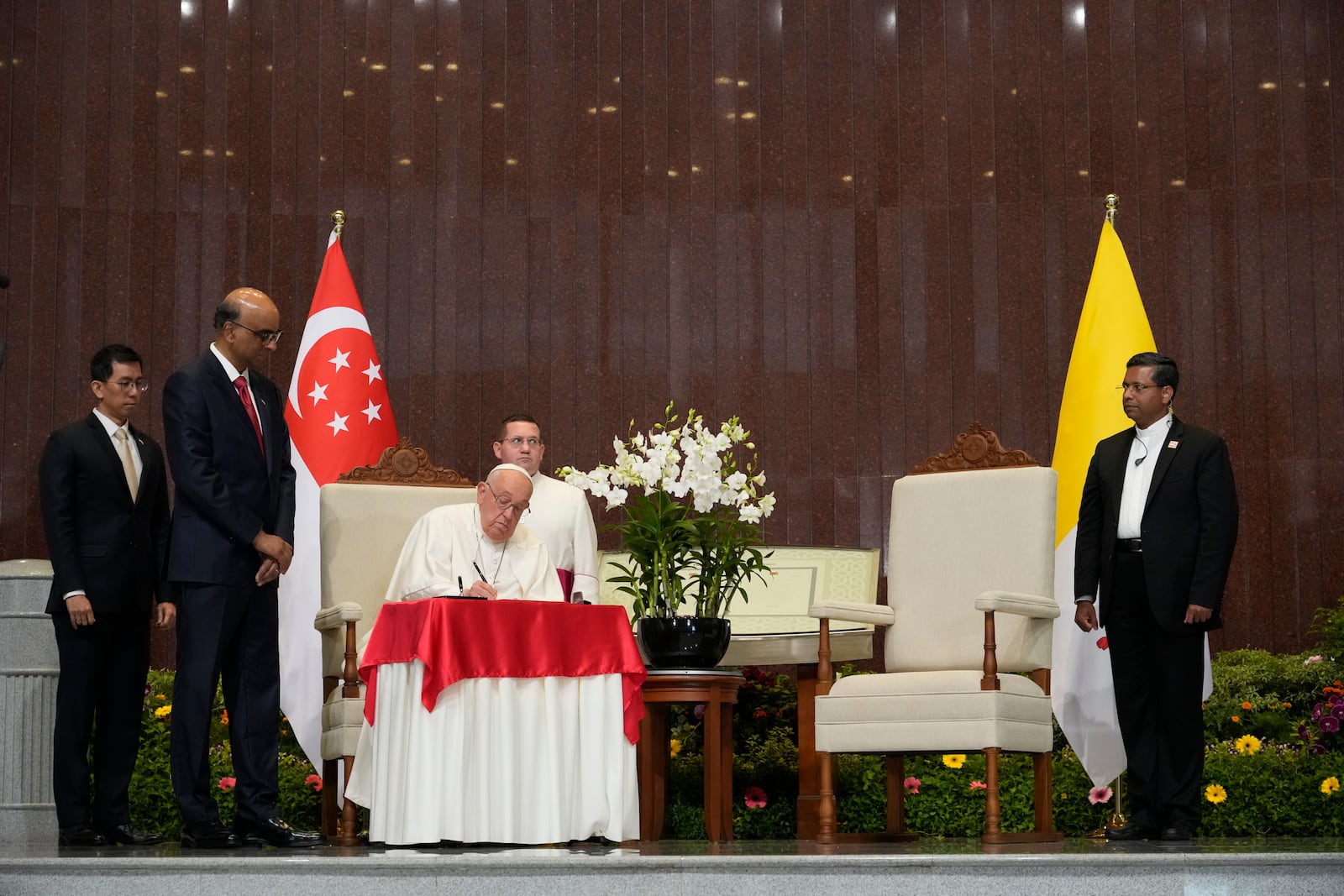 Pope Francis signs the book of honor during a welcome ceremony with the President of the Singapore Republic Tharman Shanmugaratnam, second from left, at the Parliament House in Singapore, Thursday, Sept. 12, 2024. Pope Francis flew to Singapore on Wednesday for the final leg of his trip through Asia, arriving in one of the world's richest countries from one of its poorest after a record-setting final Mass in East Timor. (AP Photo/Gregorio Borgia)