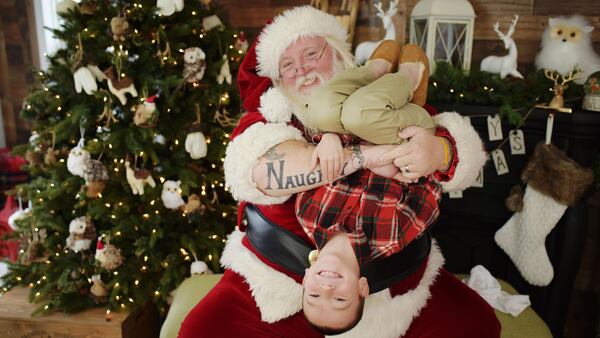 In this undated image provided by Allicia Leaper of Crush Photography, Scott Diethorne, dressed as Santa, poses for a photo with at child upside down in his arms. Diethorne, the beloved Santa with "naughty" tattooed on one arm and "nice" tattooed on the other, has been asked to tone down his typically goofy poses at a suburban Philadelphia mall, leaving some fans miffed.