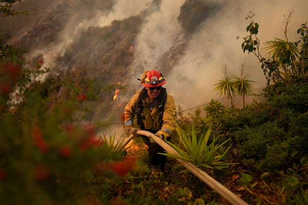 A firefighter sets up a hose while fighting the Palisades Fire in Mandeville Canyon on Saturday, Jan. 11, 2025, in Los Angeles. (AP Photo/Eric Thayer)