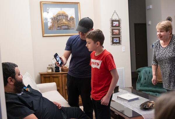 230222-Atlanta-Artem Parubets shows his son Maksym, 12, a photo of himself at work as his mother comes to take a look Wednesday evening, Feb. 22, 2023. The Parubets family, who arrived earlier this month from Ukraine, are living with Mina Youssef, left, and his wife Melissa in their Buckhead home.  Ben Gray for the Atlanta Journal-Constitution