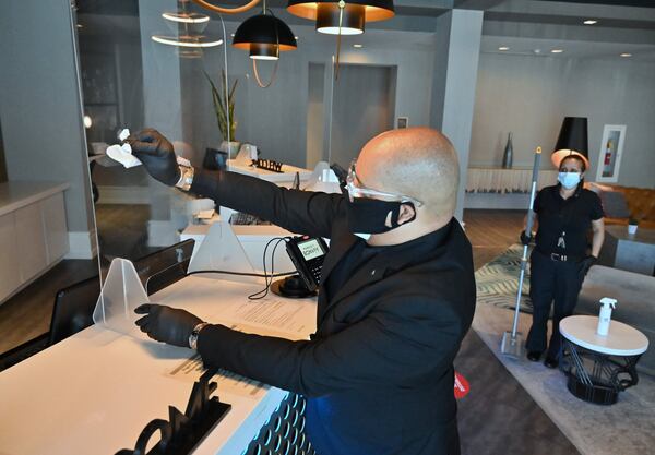 David-Michael Searcy, concierge, uses a disinfectant wipe to clean up plexiglass dividers at the front desk of W Atlanta-Buckhead on Friday, June 12, 2020. The battered hotel industry is gradually recovering, with some hotels in Atlanta reopening but occupancy rates still low. (Hyosub Shin / Hyosub.Shin@ajc.com)