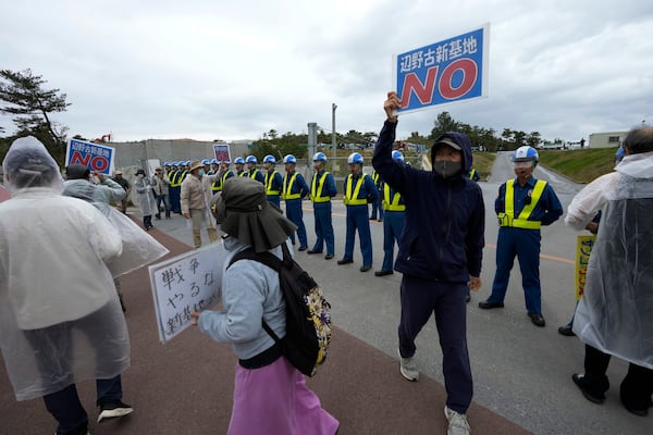 People with signs of "No, Henoko new base" and "Stop war, Don't make a new base" chant slogans against construction along Camp Schwab, a U.S. Marine Corps base, as they protest in Nago, on the main island of the Okinawa archipelago, southern Japan, Tuesday, Feb. 18, 2025. (AP Photo/Hiro Komae)