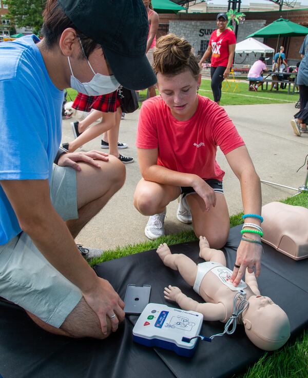 Philadelphia College of Osteopathic Medicine student Danny Kim (left) demonstrates how to perform CPR and use a defibrillator on an infant doll to Ashley Benton, 15, at the Student Docs for Shocks booth during the Suwanee Fest in Suwanee. PHIL SKINNER FOR THE ATLANTA JOURNAL-CONSTITUTION.