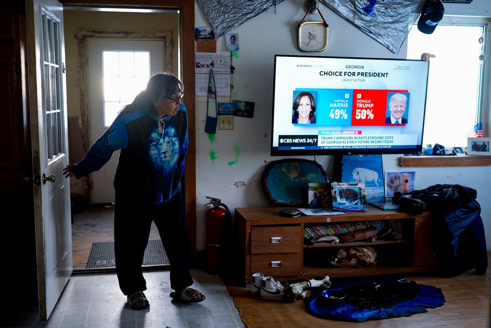 Alice Aishanna steps into her living room while a CBS News broadcast shows Democratic presidential nominee Kamala Harris and Republican presidential nominee former President Donald Trump, Tuesday, Oct. 15, 2024, at her home in Kaktovik, Alaska. (AP Photo/Lindsey Wasson)