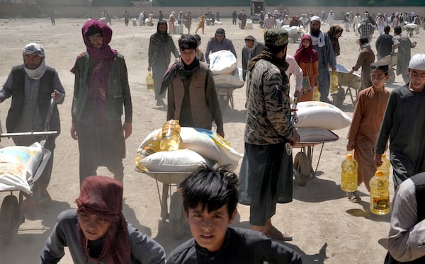 FILE - A Taliban fighter stands guard as people receive food rations distributed by a Chinese humanitarian aid group, in Kabul, Afghanistan, Saturday, April 30, 2022. (AP Photo/Ebrahim Noroozi, File)