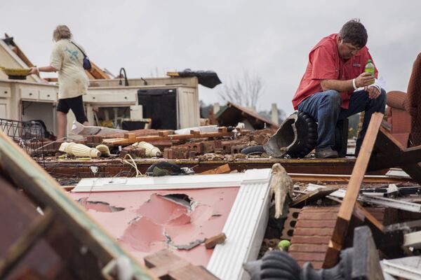 Jeff Bullard sits in what used to be the foyer of his home as his daughter, Jenny Bullard, looks through debris at their home that was damaged by a tornado Sunday in Adel. Gov. Nathan Deal declared a state of emergency in 16 counties. (Credit: Branden Camp / Associated Press)