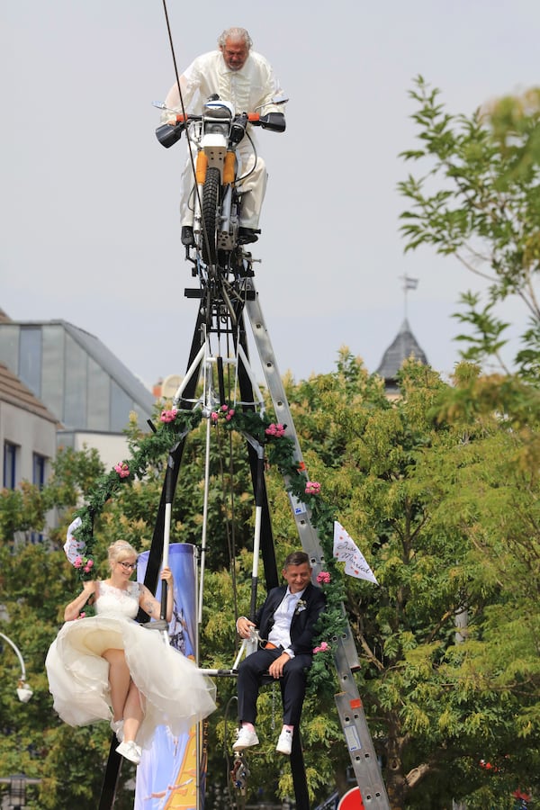 Bride Nicole Backhaus, left, and groom Jens Knorr, right, sit in a swing dangling under a motorcycle with artist Falko Traber, top, during their wedding ceremony atop a tightrope in Stassfurt, Germany, Saturday, June 16, 2018.