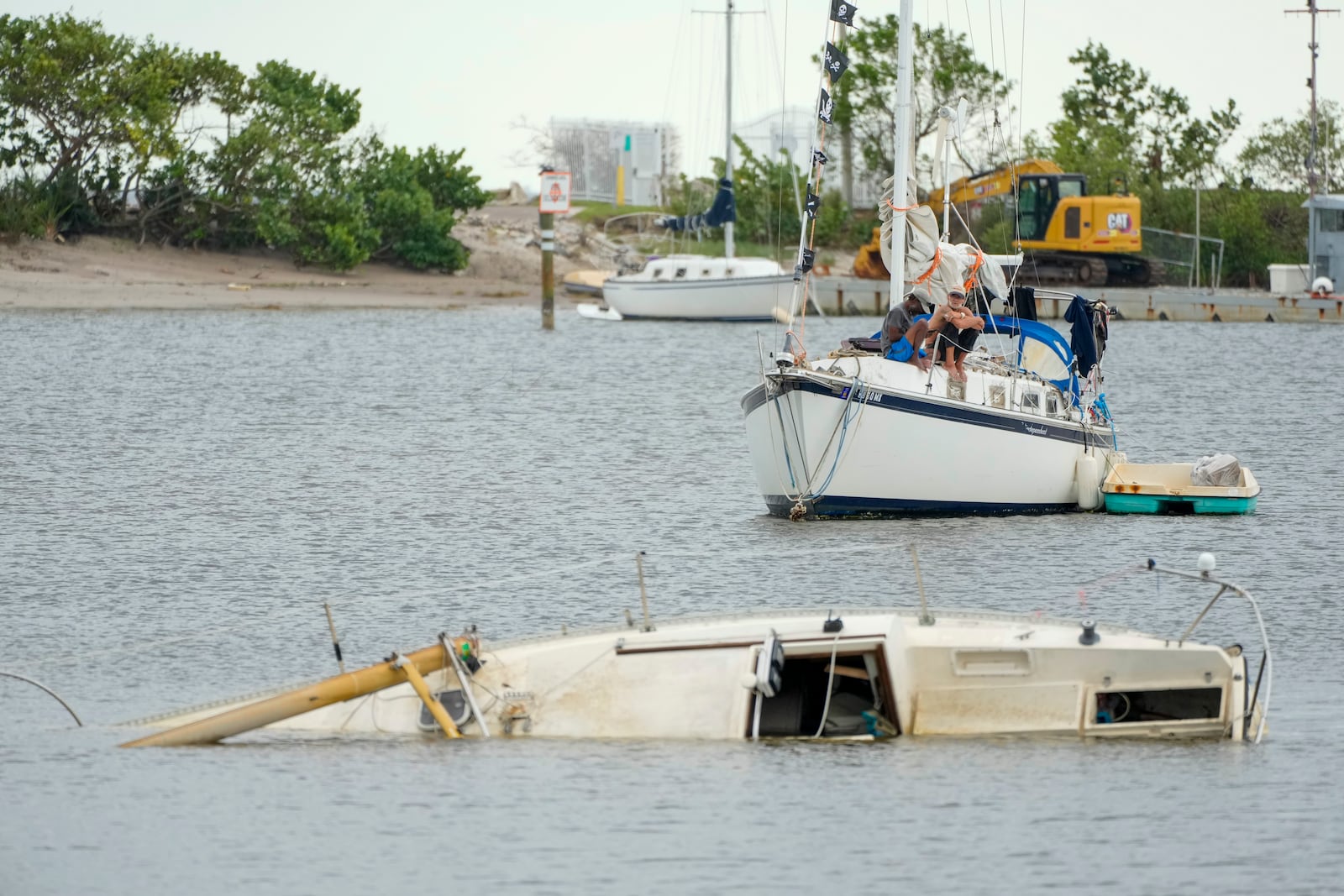 A sunken boat is seen as men sit on a sailboat in the Davis Islands Yacht Basin in Tampa, Fla., the day after Hurricane Milton hit the region, Thursday, Oct. 10, 2024. (AP Photo/Julio Cortez)