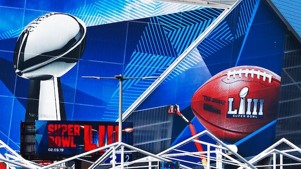 In this Jan. 17, 2019 photo, workers use a lift to install a Super Bowl 53 wrap on the outside of Mercedes-Benz Stadium as it is transformed for the big NFL football game in Atlanta.