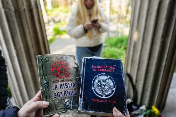 A woman holds copies of The Satanic Bible by Church of Satan founder Anton Szandor LaVey and The Bible of the Adversary by Michael Ford, before the start of a ceremony at the General Cemetery in Santiago, Saturday, Sept. 14, 2024. (AP Photo/Esteban Felix)