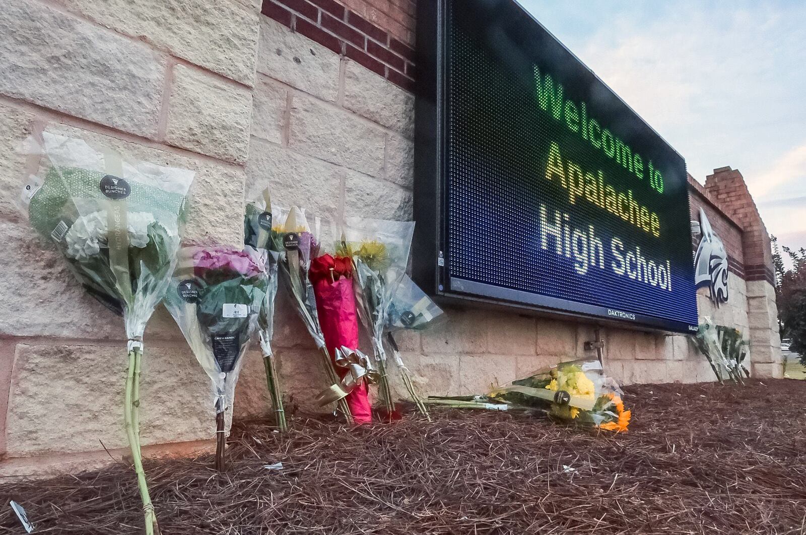 Flowers are placed at the foot of the welcome sign to Apalachee High School, where four people were killed and nine others were injured during a mass shooting. Colt Gray, a 14-year-old student, faces four murder charges in the shooting, and his father has been charged with second-degree murder. Warrants allege that he gave his son access to the semiautomatic rifle used in the shooting even though he knew the teen was a danger to himself and others. (John Spink/The Atlanta Journal-Constitution/TNS)