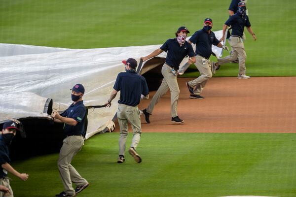 The Braves ground crew works quickly to cover the field with a rain tarp. (ALYSSA POINTER / ALYSSA.POINTER@AJC.COM)