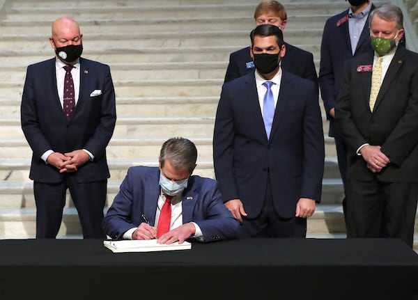 Gov.  Brian Kemp signs the amended fiscal year 2021 budget with bonuses and extra money for schools and health while Senate Majority Leader Mike Dugan, from left, Lt. Gov. Geoff Duncan and House Appropriations Chair Terry England look on. Federal spending that sent more money to Georgians helped produce the surge in tax collections that helped fund those expenditures. Curtis Compton / Curtis.Compton@ajc.com”