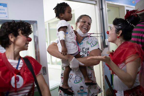 Two-year-old Maria Ysis Nascimento Figueiredo is held by her mother as she watches a clown from the "Roda de Palhacos" cultural project perform during a carnival party at the pediatric area of the Servidores do Estado Federal Hospital in Rio de Janeiro, Tuesday, March 11, 2025. (AP Photo/Bruna Prado)