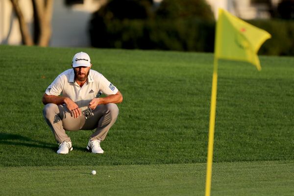 Dustin Johnson looks over his shot on the 18th green next to the Masters yellow flag during the third round of the Masters Saturday at Augusta National. (Curtis Compton / Curtis.Compton@ajc.com)

