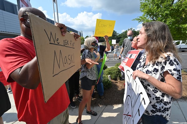 A demonstrator holds a sign that says, "We ask for mask" is confronted by outside the headquarters of the Cobb County School District on Aug. 12, 2021.(Hyosub Shin / Hyosub.Shin@ajc.com)