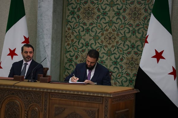 Syria's interim president Ahmad Al-Sharaa, center, signs a temporary constitution for the country in Damascus, Syria, Thursday March 13, 2025. At left foreign minister Asaad Hassan al-Shiban.(AP Photo/Omar Albam)