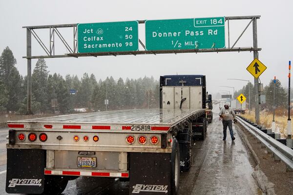 A trucker walks around their vehicle while installing snow chains during a storm Wednesday, Nov. 20, 2024, in Truckee, Calif. (AP Photo/Brooke Hess-Homeier)