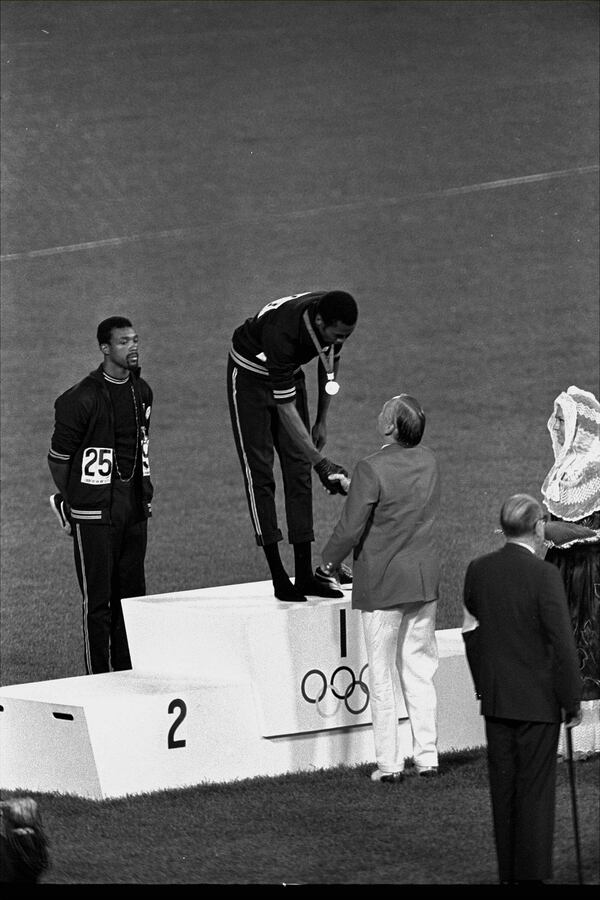 FILE - With his hand covered in a black glove, Tommie Smith of the U.S. accepts congratulations from Lord David Burghley after being awarded the gold medal for winning the 200-meter dash at the Summer Olympic Games in Mexico City on Oct. 16, 1968. (AP Photo/RW, File)