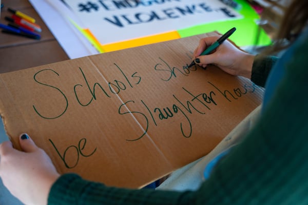 A student makes a sign out of a piece of cardboard that reads "Schools shouldn't be slaughterhouses," during a rally at J.B. Williams Park on Friday, Sept. 20, 2024. (Olivia Bowdoin for the AJC)