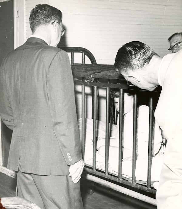 Visitors to Milledgeville State Hospital observe a small boy restrained in a metal cage in the 1940s. AJC FILE