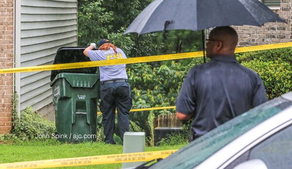 A Gwinnett County police investigator looks inside a trashcan for any clues that could lead them to a motive or a suspect in a fatal shooting Thursday. JOHN SPINK / JSPINK@AJC.COM