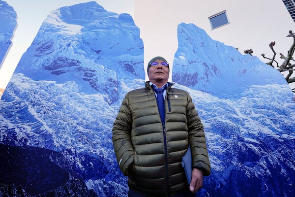 The plaintiff Peruvian farmer Luciano Lliuya stands in front of glacier pictures held by activists at the Higher Regional Court in Hamm, Germany, for a first hearing of his climate damages case against the German energy company RWE for its carbon emissions, which may have been contributing to the melting of a nearby glacier that could flood his home, Monday, March 17, 2025. (AP Photo/Martin Meissner)