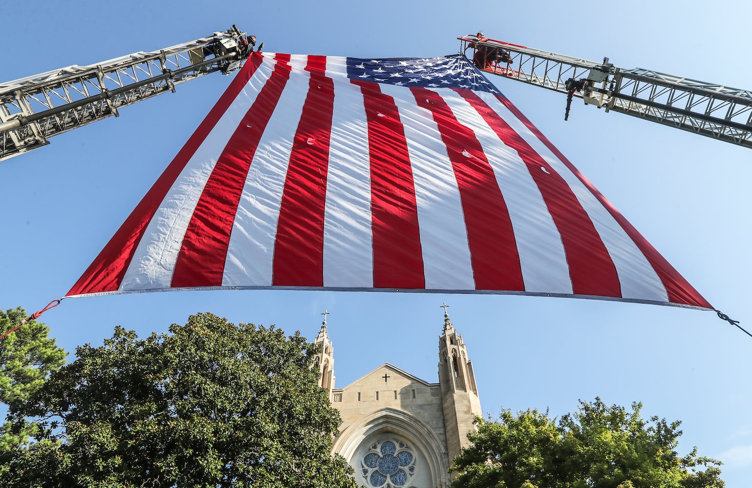 September 11, 2023 Atlanta: Atlanta firefighters post  a giant American flag between ladders at the Cathedral of Christ the King. Atlanta police and firefighters were in attendance on Monday, September 11, 2023 at the Cathedral of Christ the King, 2699 Peachtree Road, NE in Buckhead in observance of the Blue Mass. The annual Mass honors public safety officials and first responders. City of Atlanta Mayor, Andre Dickens, along with police, fire officials and honor guards participated in the solemn Mass led by Rector, Monsignor Francis G. McNamee. Wreaths were posted in front of the of the church, honoring those who lost their lives on Sept. 11, 2001. The Blue Mass tradition began in 1934, when a priest from the Archdiocese of Baltimore, Father Thomas Dade formed the Catholic Police and Firemen’s Society. (John Spink / John.Spink@ajc.com)

