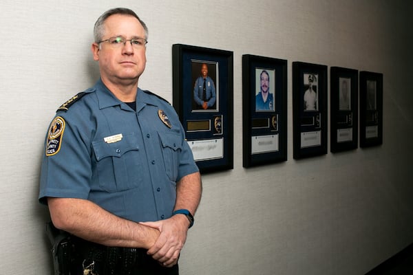 Now-former Gwinnett County police Chief Butch Ayers poses with memorials of the five officers who lost their lives in the line of duty at the Gwinnett County Police headquarters in Lawrenceville. Ayers retired Nov. 15, after five years in charge and more than three decades with the department. (Photo/Rebecca Wright for the Atlanta Journal-Constitution)