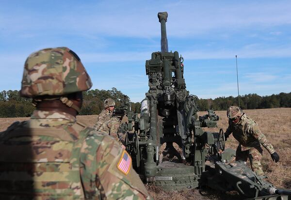 Georgia National Guardsman Ryan McBride, left, looks on as his fraternal twin, Matthew, drills with a howitzer during training at Fort Stewart in December. Curtis Compton/ccompton@ajc.com