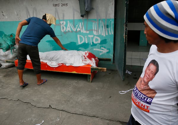 FILE - A man wearing a campaign t-shirt of President Rodrigo Duterte, watches as a relative touches the body of a man killed allegedly in a "buy-bust" operation at a Muslim community in Manila, Philippines, Sept. 16, 2016. (AP Photo/Bullit Marquez, File)