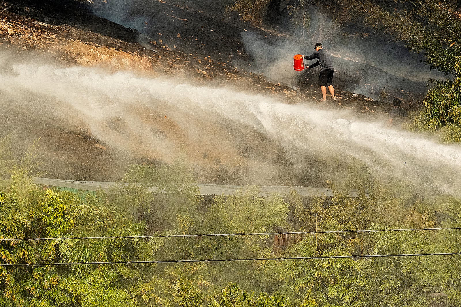 A person dumps water on a grass fire burning above Interstate 580 in Oakland, Calif., Friday, Oct. 18, 2024. (AP Photo/Noah Berger)