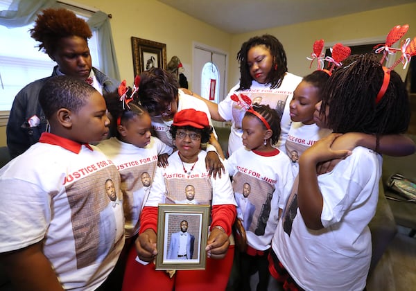 013121 Stone Mountain: Janet Morris (center) holds a picture of her son Jireh Morris, who was killed in a December shooting at a DeKalb County apartment complex, while being consoled by family members wearing justice shirts bearing Jireh’s picture at the family home on Sunday, Jan. 31, 2021, in Stone Mountain. From left are  grandchildren Nolan Demond Evans, daughter Brittany Michelle Morris, Jana Marie Evans, mother Jeanette Ingersoll, daughter Lana Marie Starks, Zoey Marie Starks, Laia Cristina-Janet Starks, and Skylar Michell Starks.    Curtis Compton / Curtis.Compton@ajc.com”