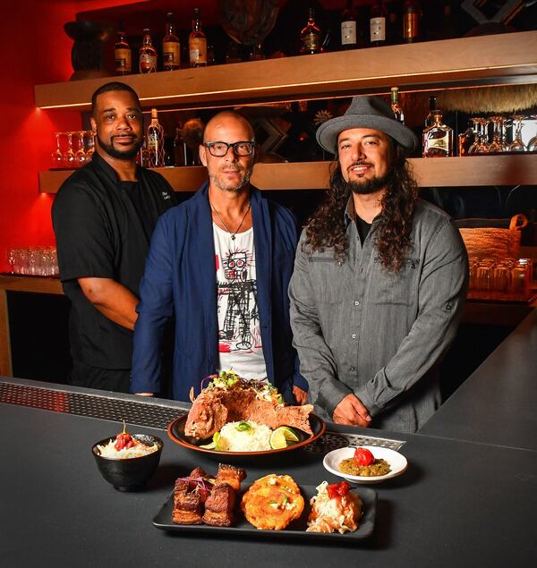 Executive chef Christian Lucke Bell (from left) and Rock Steady co-founders Joe Russo and Jacob Thomas are shown with some Haitian dishes. Thomas’ mother is from Haiti, so he grew up eating Caribbean cuisine. They’re standing in front of the rum bar inside the West Midtown restaurant, which hosts over 50 different types of rum. STYLING BY CHRISTIAN LUCKE BELL / CONTRIBUTED BY CHRIS HUNT PHOTOGRAPHY