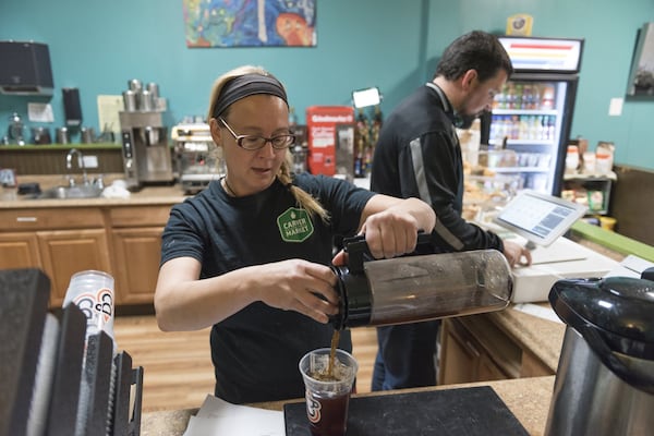 Kasia Jakubowski (center), 46, a barista at Community Grounds Cafe, prepares an iced coffee while Jeff Delp (right), executive director of Carver Neighborhood Market, briefly helps at the register. Community Grounds Cafe is connected to the store and has seen an influx of customers as the variety of products they offer increases. DAVID BARNES / SPECIAL