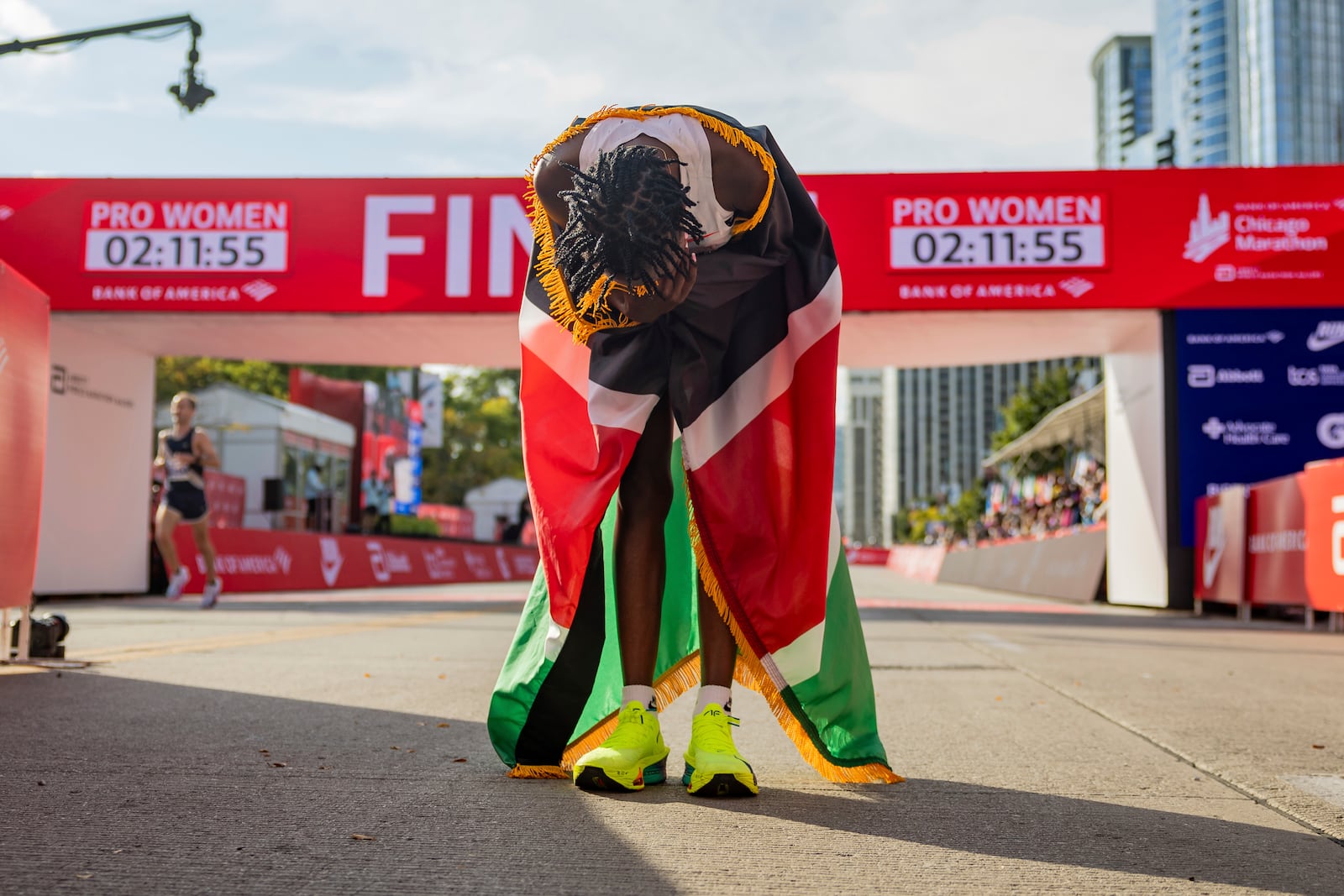 Ruth Chepngetich, from Kenya, lowers her head while wearing the Kenyan flag after crossing the finish line of the Chicago Marathon to win the women's professional division and break the women's marathon world record in Grant Park on Sunday, Oct. 13, 2024. (Tess Crowley/Chicago Tribune via AP)