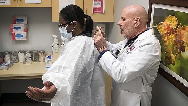 Dr. John Destito, at right, places a protective covering on office manager Kay Hayes at their American Family Care clinic in Buckhead. The two were going through a training for coronavirus procedures. (PHOTO by ALYSSA POINTER/ALYSSA.POINTER@AJC.COM)