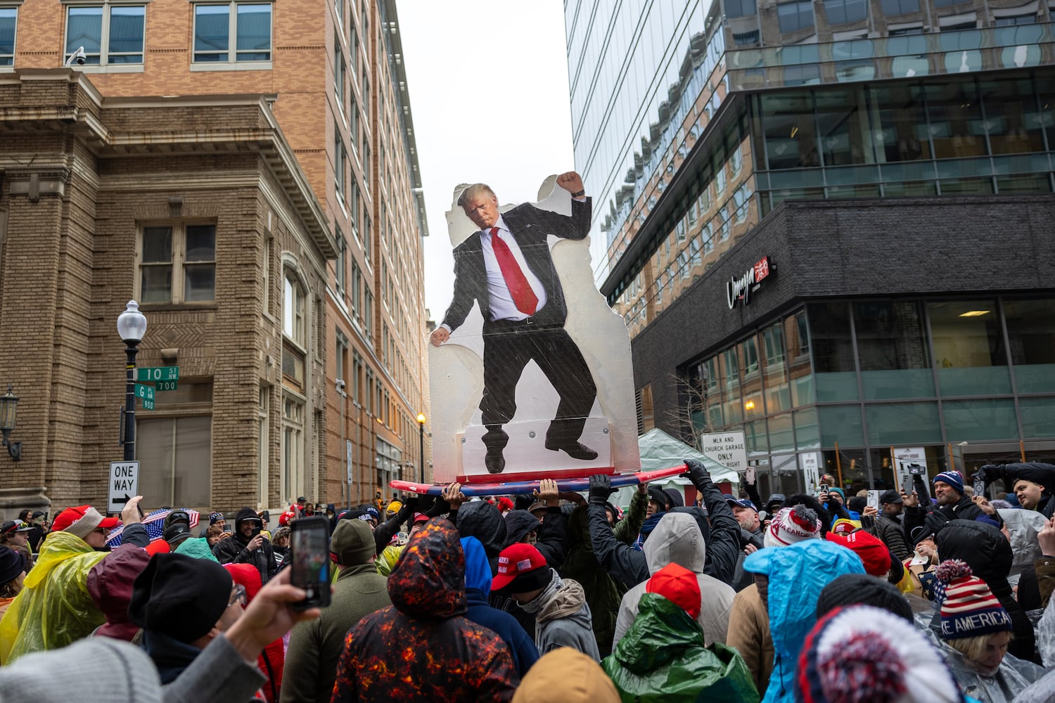 People waiting to enter a Trump rally at Capital One Arena in Washington, D.C. pass around a Trump cutout on a surfboard on Sunday, January 19, 2025, one day before Donald Trump’s inauguration. Attendees said the cutout was surfing the red wave to drain the swamp. (Arvin Temkar / AJC)