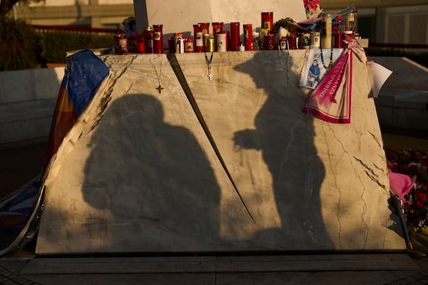 A woman is silhouetted as she holds a Christian rosary after praying next to the statue of Pope John Paul II placed outside the Agostino Gemelli hospital in Rome, Thursday, March 6, 2025. (AP Photo/Francisco Seco)