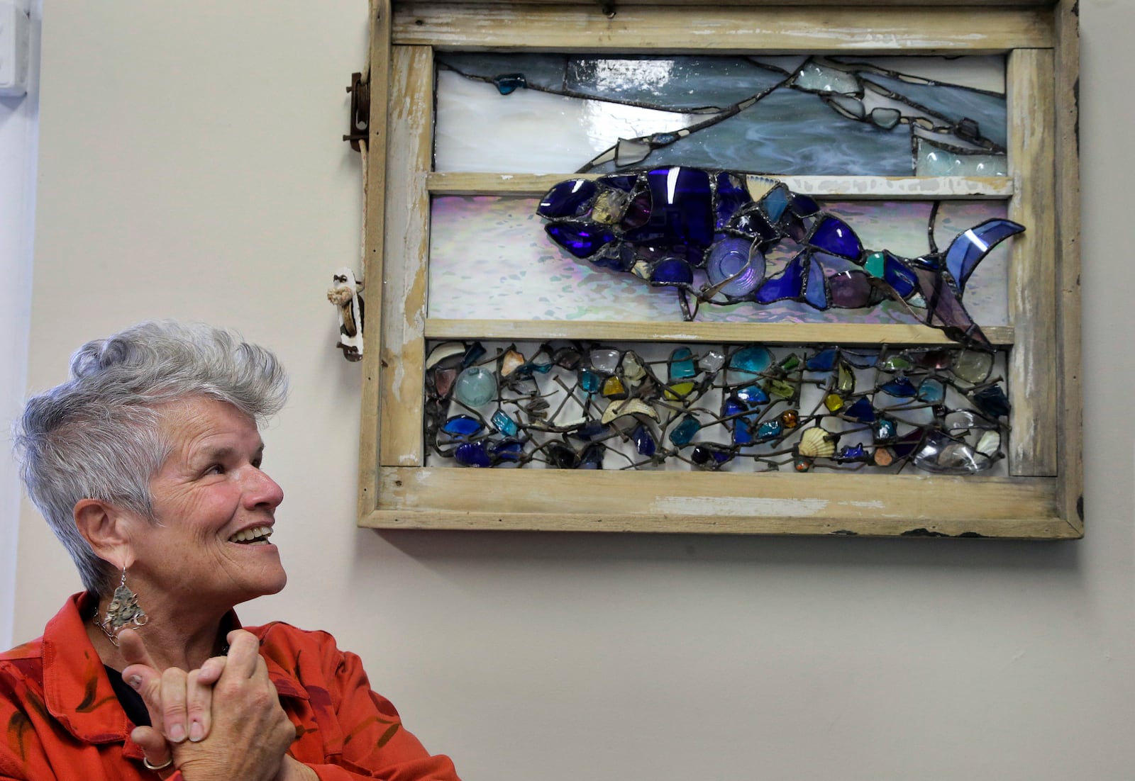 In this Monday, May 8, 2017 photo artist Donna Mahan, of Truro, Mass., talks about her art object called "Safeguarding," right, at the John F. Kennedy Hyannis Museum in Hyannis, Mass. The art object was made from materials including a hand-crafted window and antique nails removed during a recent renovation of John F. Kennedy's summer home. The items removed from the house were preserved and offered to Cape Cod artists who in turn fashioned them into artwork. Mahan's "Safeguarding" also includes repurposed glass that did not come from the Kennedy home. (AP Photo/Steven Senne)