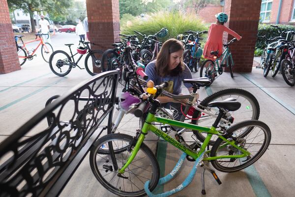 Tasha Rodriguez locks her daughter’s bike by a bench after all the bike racks filled up during the weekly Parkside Elementary School “bike bus” ride Friday, Sept. 20, 2024, in Atlanta. Ben Gray for the Atlanta Journal-Constitution