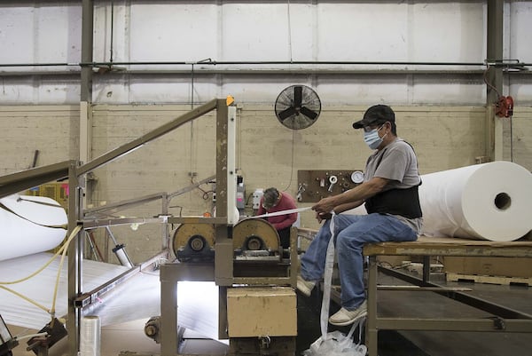 Joel Arenes cuts off extra material from the manufactured gown composite material at Fabric Sources International, LLC in Dalton on April 8, 2020. Fabric Sources International, LLC is creating gown composite material for manufactures to create makeshift medical gowns for healthcare workers during the COVID19 pandemic. (ALYSSA POINTER / ALYSSA.POINTER@AJC.COM)